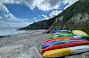 Fargerike kajakkar og sup-brett på ei strand i Guernsey.