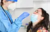 Nurse in a protective suit takes a nasal swab sample from a young female patient. COVID-19 concept.
